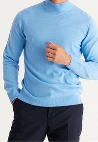 Ljusblå polotröja i mjukt, slätt tyg. Har ribbade ärmslut och nederkant. Bärs med mörka byxor; passformen är avslappnad och ledig.