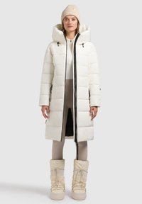 White puffer coat with a hood and black zipper, featuring large horizontal baffles. Paired with beige snow boots and coordinating tights.