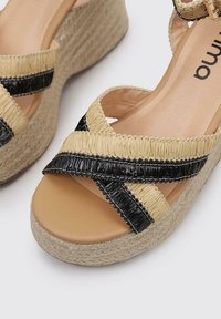 Sandalias de cuña con una suela de yute tejido natural, tiras cruzadas en negro y beige, y un interior suave con un diseño de punta redonda.