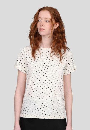 T-shirt crème à manches courtes avec des pois noirs. Encolure ronde, coupe décontractée, texture en coton lisse, ourlet au niveau des hanches.
