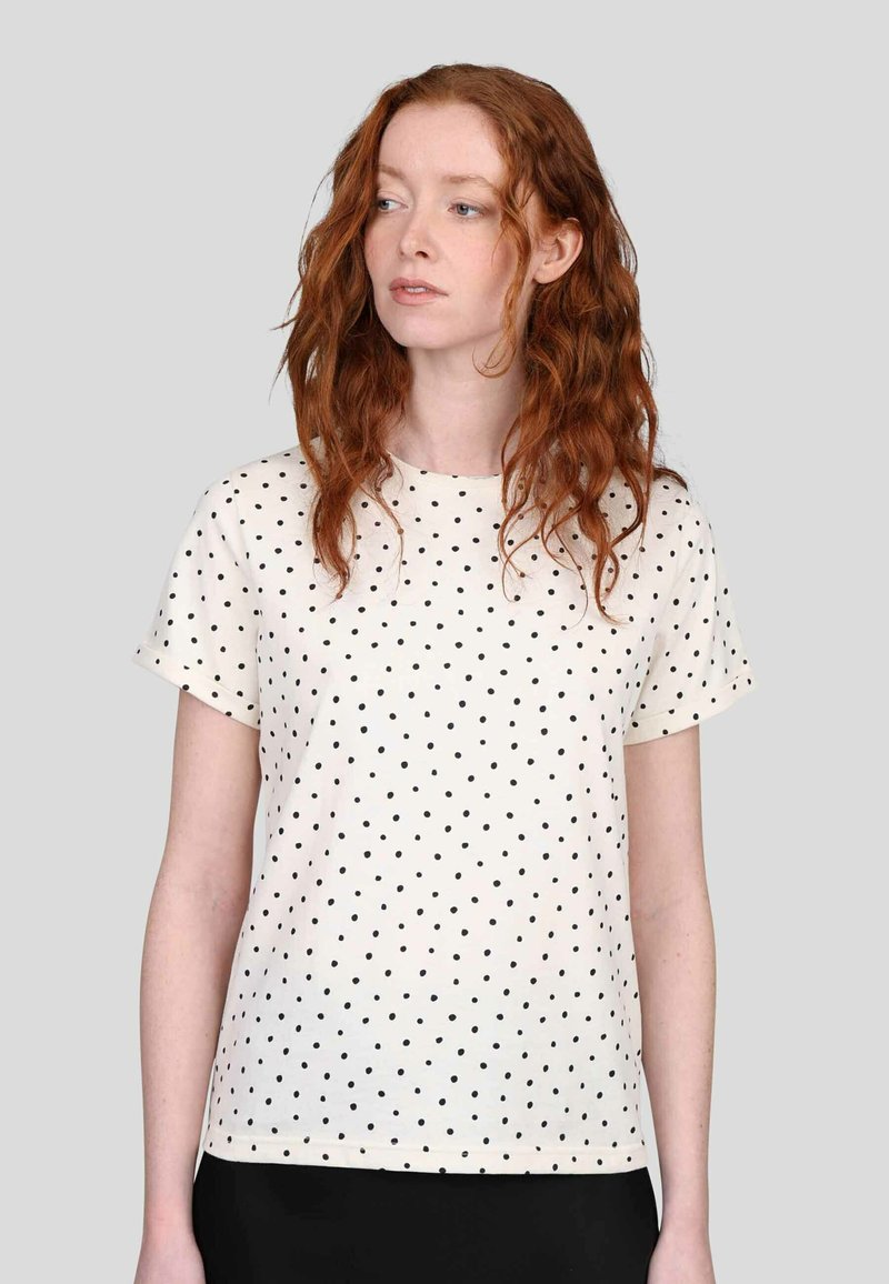 T-shirt crème à manches courtes avec des pois noirs. Encolure ronde, coupe décontractée, texture en coton lisse, ourlet au niveau des hanches.