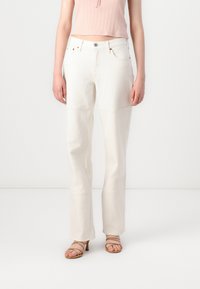 White denim pants with a straight-leg design, featuring seams and stitched detailing. Paired with a light pink ribbed top and strappy sandals.