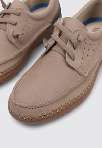 Chaussures en cuir beige avec une finition texturée, bout rond, détail perforé sur les côtés et lacets assortis. Semelle en caoutchouc avec des accents de coutures.