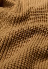 Texturiertes braunes Gewebe mit einem Waffelmuster und subtilen gerippten Details, das ein weiches und gemütliches Aussehen erzeugt.