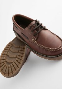 Braune Lederschuhe mit runder Zehenform, kontrastierenden Nähten, Schnürdesign und strukturiertem Gummisohle mit einem Griffmuster.
