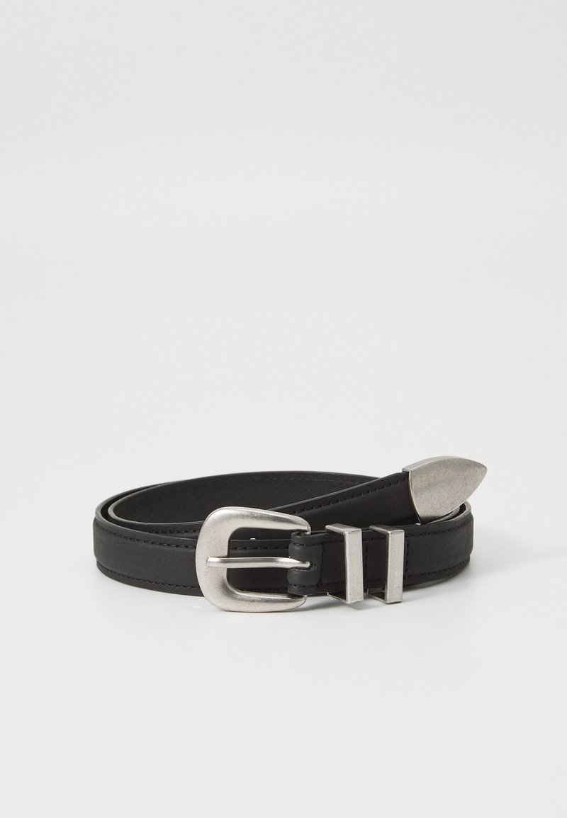 Ceinture en cuir noir avec boucle métallique argentée, deux passants de ceinture et une pointe en métal, roulée sur un fond blanc.