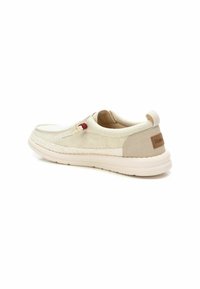 Zapatos beige sin cordones con una parte superior de lona texturizada, suela de goma contrastante y un detalle trenzado a lo largo de la suela. Presenta un pequeño parche con el logo.