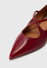 Burgundy leather flats with a pointed toe, featuring crisscross straps and a smooth texture. Interior is tan with a simple design.