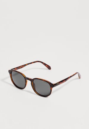 Lunettes de soleil à motif écaille avec verres polarisés foncés et branches fines reposant sur un fond blanc.