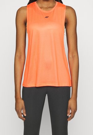 Vrouw draagt een feloranje mouwloos sporttopje en donkere aansluitende legging, staande tegen een eenvoudige lichte achtergrond.