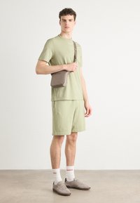 Light green cotton t-shirt with embossed logo, matching shorts, grey bag with logo, white socks with red text, and grey sneakers.