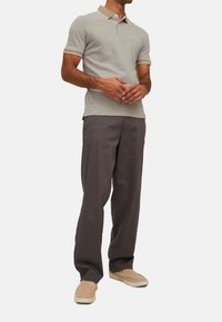 Lichtgrijs polo-shirt met een beige kraag, gecombineerd met loszittende donkergrijze broek en beige instapschoenen. Minimale branding zichtbaar.
