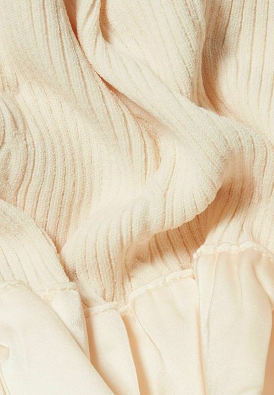 Tissu beige pâle, côtelé, avec une surface douce et texturée ; bord froncé ; détail en satin lisse contrastant avec les sections côtelées.