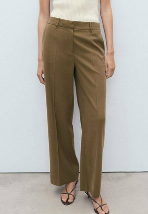 Pantaloni color marrone su misura con un design a gamba dritta, caratterizzati da pieghe frontali e una texture liscia. Abbinati a sandali con cinturini.