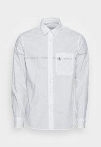 Vit långärmad skjorta i bomull med knäppning framtill, med en bröstficka på vänster sida och upprepade "Calvin Klein Jeans"-logotyper.