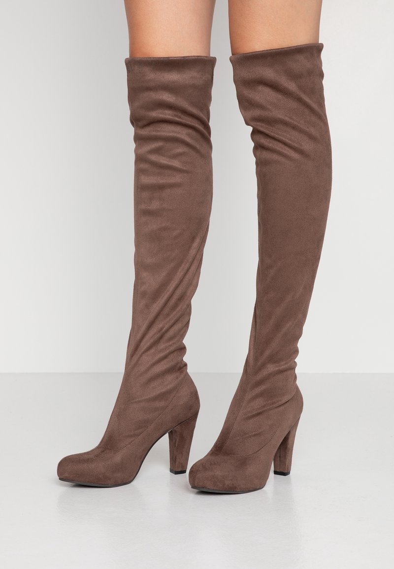 Botas marrones hasta la rodilla hechas de un material aterciopelado, con un diseño arrugado y una puntera redonda, que cuentan con un tacón ancho alto.