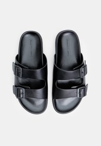 Sandale negre cu două catarame ajustabile, fabricate dintr-un material sintetic neted. Design cu vârf deschis și tălpi plate. Formă minimalistă și funcțională.