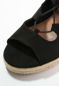 Sandaletta con zeppa in suede nera, con punta aperta, design con ritagli e suola in corda di juta. Il tacco misura circa 7,5 centimetri.