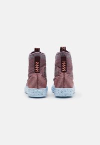 Wysokie buty sportowe z fakturowaną burgundową cholewką, kontrastową jasnoniebieską podeszwą i dwoma uchwytami. Widoczne akcenty pomarańczowych szwów.