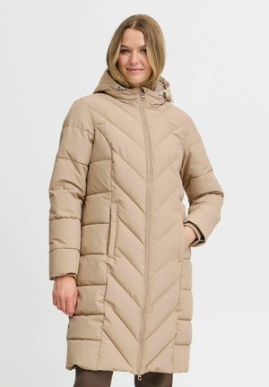 Manteau long beige en duvet avec capuche, doté d'une fermeture éclair à l'avant, d'un design matelassé en chevrons et de poches latérales. Texture lisse avec un aspect chaud et isolé.