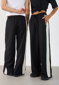 Melni platā stila bikses ar beigu sānu svītrām un tirkīza akcentiem. Mīksts audums, elastīga josta un kabatas abās pusēs.