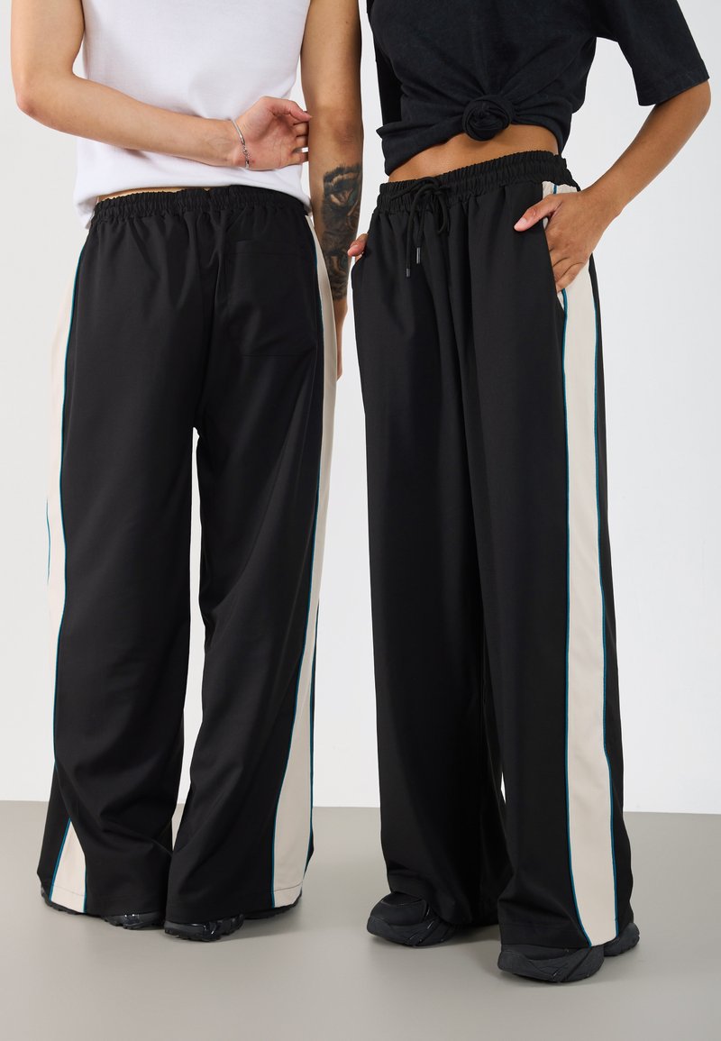 Crne široke hlače s bež bočnim prugama i tirkiznim akcentima. Mekani materijal, elastičan struk i džepovi s obje strane.