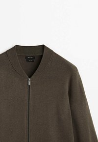 Pull marron à fermeture éclair avec col côtelé et manches longues, présenté sur un fond blanc uni.