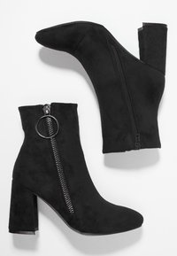 Botas de tobillo de ante negro con un tacón grueso, cremallera lateral con un tirador circular y un diseño de punta suave.