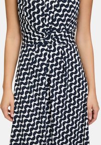 Marineblaues und weißes gemustertes Kleid mit wellenförmigem Design, Falten am unteren Ende und einer geknoteten Detail an der Taille für zusätzliche Struktur.