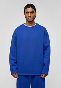 Koninklijk blauwe oversized sweatshirt met een ronde hals en verlaagde schouders, gemaakt van zachte stof. Gecombineerd met bijpassende blauwe onderkleding.