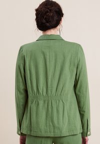 Giacca verde a maniche lunghe con vita stretta, realizzata in tessuto testurizzato. Presenta un colletto a punta e polsini con bottoni.