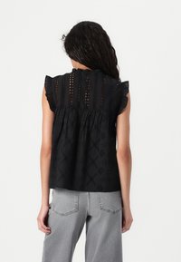 Top nero a maniche corte con scollatura arricciata, dettagli in pizzo e vestibilità comoda. Abbinato a jeans grigi a gamba larga.