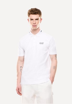 Polo bianco a maniche corte, con due bottoni e dettagli neri sul colletto. Logo EA7 stampato in grigio sul lato sinistro del petto.