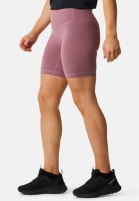 Lyserøde sportsshorts lavet af strækbart materiale, med høj talje og glatte sømme. Bæres med sorte løbesko.
