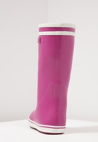 Rosa gummistövlar med en slät yta, vita accentstrimmor upptill och på sulan, samt en märkestagg på sidan.