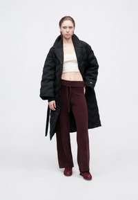 Čierny prešívaný puffer kabát, béžový skrátený top, burgundské nadýchané široké nohavice a červené topánky, prezentované na jednoduchom bielom pozadí.