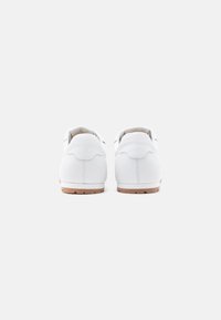Paire de baskets en cuir blanc vues de dos, montrant des semelles en caoutchouc beige et des détails de couture minimalistes sur un fond uni.
