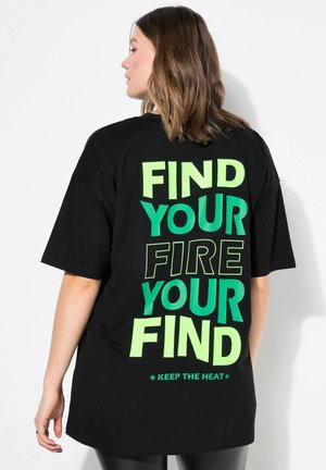 Camiseta negra de gran tamaño con un texto en verde y turquesa en la parte posterior que dice "ENCUENTRA TU FUEGO TU ENCUENTRO." Mangas cortas.