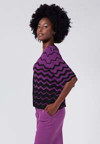 Lila och svart zigzag-mönstrad stickad topp med korta ärmar, i kombination med lila byxor. Slät textur och avslappnad passform.