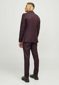 Costume bordeaux avec une coupe ajustée, présentant une fente simple à l'arrière et une texture lisse, assorti à des chaussures noires.