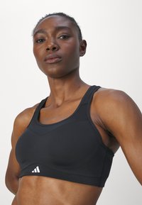 Svart treningstop med rund hals, racerback-design, glatt stoff og en liten hvit logo. Teksturert, elastisk bånd nederst.