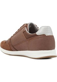 Zapatilla de cuero marrón y ante con suela de goma blanca, parte superior texturizada y un acento de cuero plateado en el talón.