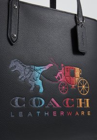 Sort tekstureret lædertaske med et flerfarvet billede af en dinosaur og en vogn, med teksten "COACH LEATHERWARE" i fed skrift.