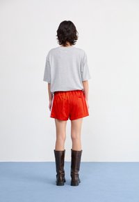 Grå oversize t-shirt, röda linjerade shorts och knähöga bruna läderstövlar, visade bakifrån mot en enfärgad bakgrund.