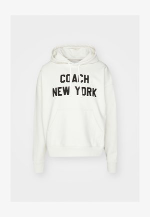 Bela kapuca z napisi "COACH NEW YORK" v bold črni barvi, kenguru žep, ribana manšeta in kapuca z vrvico. Mehka tekstura tkanine.