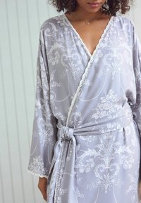 Robe floreale grigia con una texture morbida, dotata di scollatura a V, maniche lunghe e una cintura da annodare, rifinita con pizzo bianco lungo i bordi.