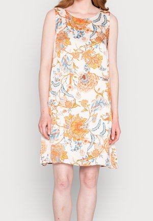 Ærmeløs knælængde kjole med orange, blå og beige blomsterprint på hvid baggrund båret af en stående person.
