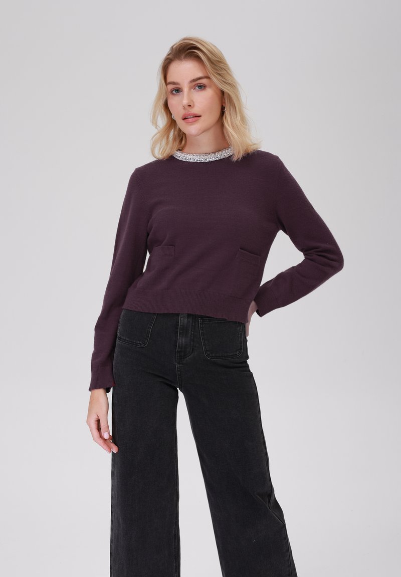 Corto maglione viola con un colletto argento testurizzato, dotato di due tasche frontali. Abbinato a jeans neri a gamba larga a vita alta.