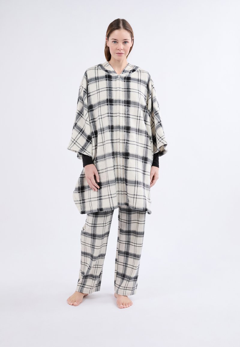 Poncho à carreaux en flanelle crème et noire avec une capuche ; assorti à un pantalon à carreaux. Les deux articles ont une coupe décontractée et une texture douce.