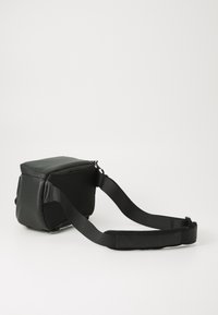 Černá, obdélníková crossbody taška s hladkým povrchem a síťovanou boční kapsou. Má pevný popruh a zipové zapínání. Lze nastavit pro pohodlí.